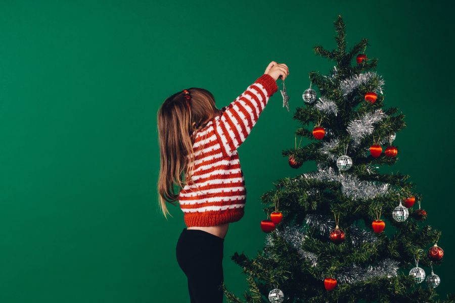 little girl in red and white sweater decorating Christmas tree on green background