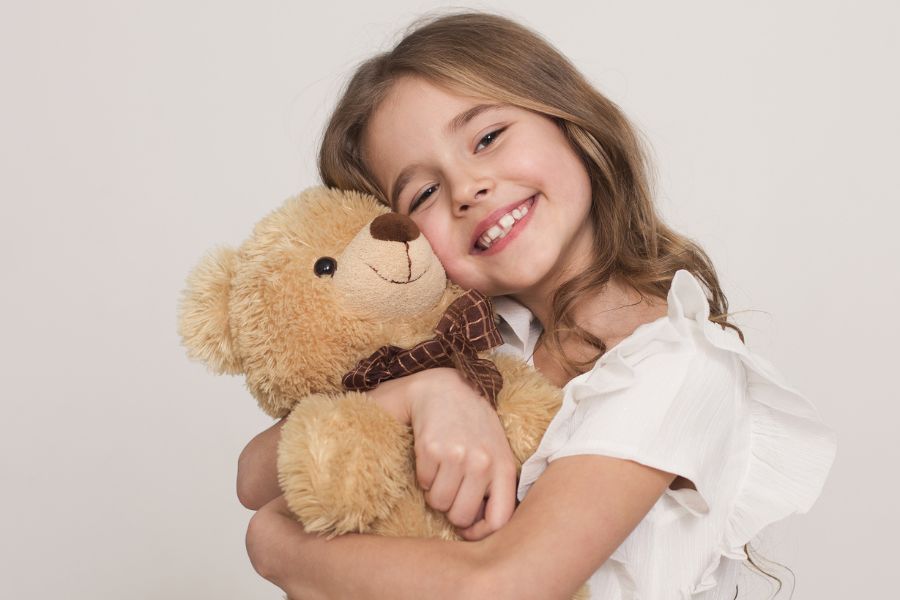 little girl snuggling teddy bear, smiling